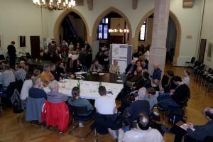 Bürger und Fachleute sitzen an einem großen Tisch im Saal des Volksbades und diskutieren verschiedene Themenzur Zukunft der Stadt Jena