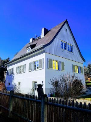 weißes Haus mit schwarzem Dach und hellen Fensterläden vor blauem Himmel