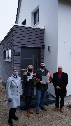 Vier Menschen vor einem Haus mit grau-weißer Fassade bei der Übergabe einer Urkunde und Plakette als Anerkennung zum Fassadenpreis