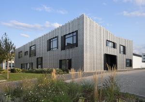 Multifunktionsgebäude mit hellgrauer Fassade aus Metall, im Vordergrund eine Grünfläche und Bäume