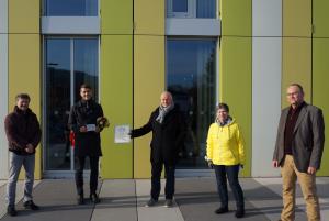Fünf Menschen vor einer grün-weißen Fassade bei der Übergabe einer Urkunde und einer Plakette als Würdigung zum Jenaer Fassadenpreis 2020e Plakette als Wü