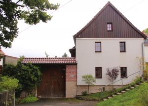 Haus mit heller Wandfarbe, Holzgiebel und Hoftor, im Vorgrund Grünfläche und Straße