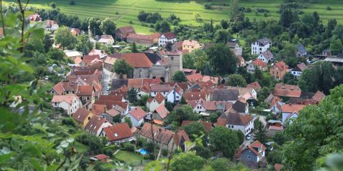 Blick auf den ländlichen Ortsteil Ziegenhain. Zu sehen ist eine Ortschaft mit dicht stehenden Häusern und roten Ziegeldächern. Der Ort ist umgeben von viel Grün (Wiesen, Bäumen und Sträuchern).