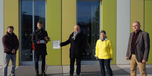 Fünf Menschen vor einer grün-weißen Fassade bei der Übergabe einer Urkunde und einer Plakette als Würdigung zum Jenaer Fassadenpreis 2020e Plakette als Wü