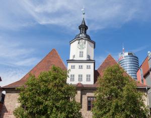 Blick vom Markt auf ein Gebäude mit Turm in der Mitte, das Historische Rathaus Jenas, im Vordergrund zwei Bäume