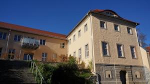 Wohnhaus mit gelber Fassade und rotem Dach mit blauem Himmel, im Vordergrund ein Garten