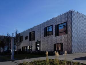 Multifunktionsgebäude mit einer Fassade aus hellem Metall vor blauem Himmel, im Vordergrund Bäume und Grünflächen