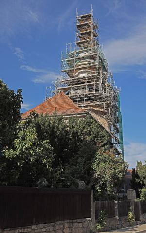 Man sieht hier die mit einem Baugerüst eingerüstete Kirche Ammerbach mit Bäumen im Vordergrund und die Kirche selbst im Hintergrund.