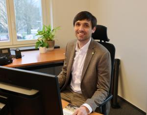 Dezernet Dirk Lange sitzt an einem Schreibtisch. Im Hintergrund ein Fenster, im Vordergrund ist der Teil des Bildschirmes zu sehen