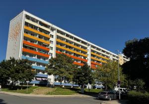 Wohnbaublocks in Plattenbauweise mit farblich gestalteten Balkonanlagen in blau, rot und gelb, im Vordergrund Bäume und Gehwege