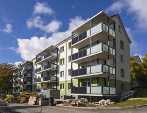 Wohnblock in Plattenabuweise mit Balkonen mit integrierten Photovoltaik-Elementen vor blauem Himmel mit kleinen Wolken