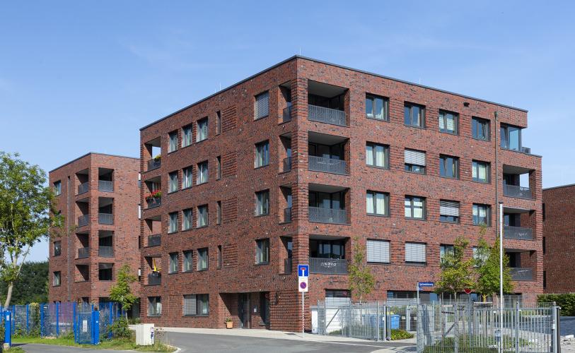 Haus mit Klinkerfassade und Fensterelementen vor blauem Himmel, im Vordergrün Grünflächen