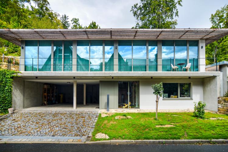 Moderner Neubau eines Wohnhauses mit massivem Erdgeschoss und darüber schwebenden Obergeschoss aus Glas, welches mit der Rückseite in den Hang gebaut ist