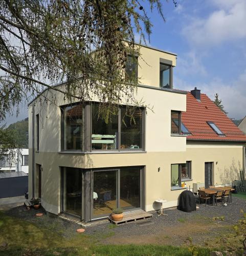 Zweieinhalb geschossiger Anbau an ein Einfamilienhaus mit heller Fassde, großen Glaselementen und zurückgesetztem Dachgeschoss