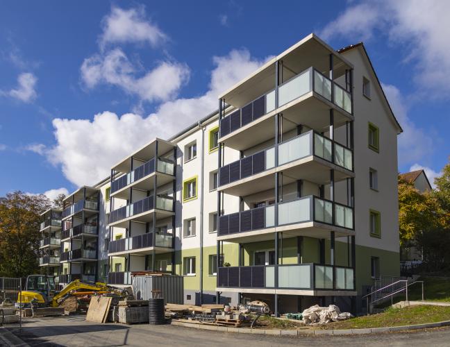 Wohnblock in Plattenabuweise mit Balkonen mit integrierten Photovoltaik-Elementen vor blauem Himmel mit kleinen Wolken