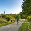 Blick auf einen Radweg mit einem Radfahrer sowie einer Joggerin mit Hund, im Hintergrund ist der Kirchturm von Kunitz zu sehen