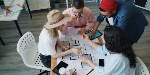 Eine Gruppe sitzt zusammen an einem Tisch und arbeitet zusammen an einem Grundriss.