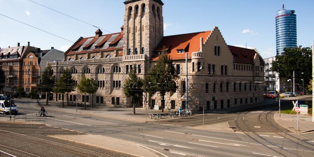 Blick vom Paradiesbahnhof auf das historische Volksbad und den JenTower mit blauem Himmel, im Vordergrund Straßenbahnschienen