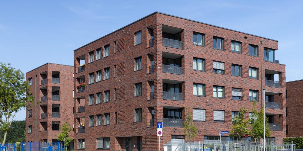 Haus mit Klinkerfassade und Fensterelementen vor blauem Himmel, im Vordergrün Grünflächen