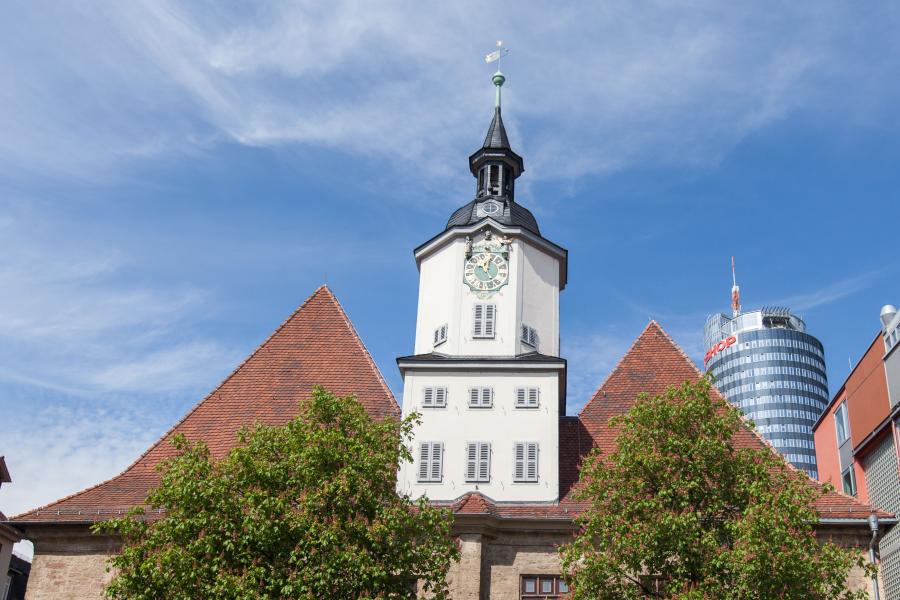 Blick vom Markt auf ein Gebäude mit Turm in der Mitte, das Historische Rathaus Jenas, im Vordergrund zwei Bäume