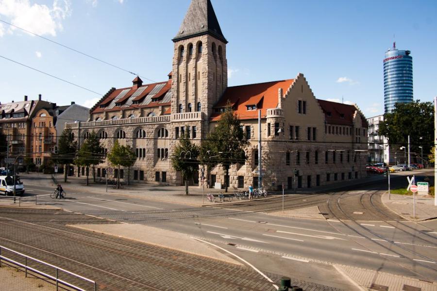 Blick vom Paradiesbahnhof auf das historische Volksbad und den JenTower mit blauem Himmel, im Vordergrund Straßenbahnschienen
