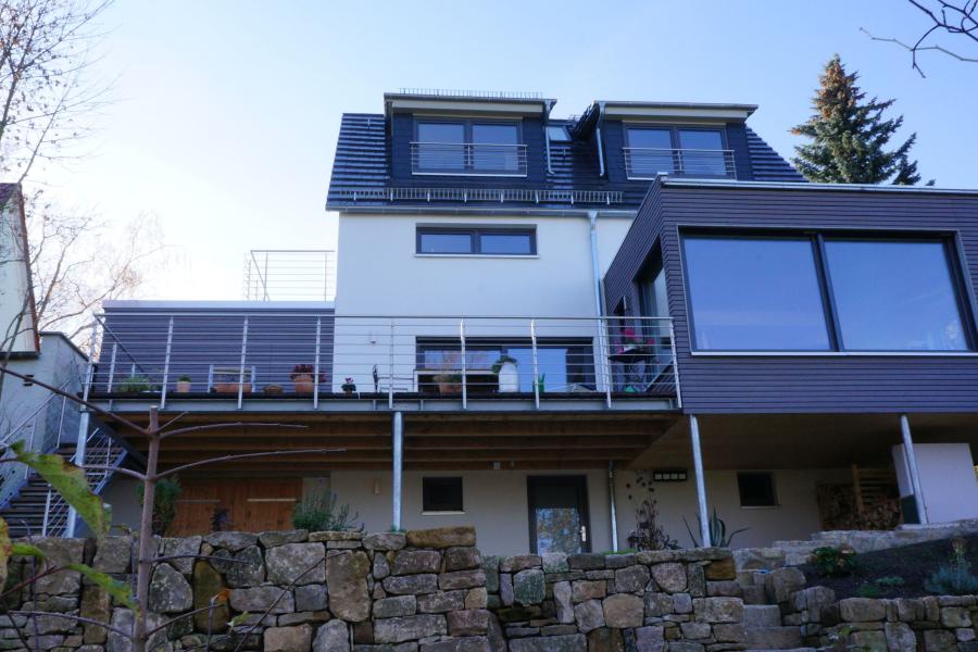 Haus mit grau-weißer Fassade auf einer Mauer aus Natursteinen