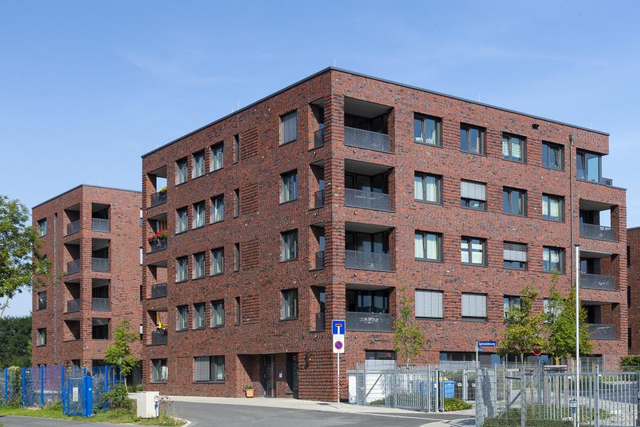 Haus mit Klinkerfassade und Fensterelementen vor blauem Himmel, im Vordergrün Grünflächen