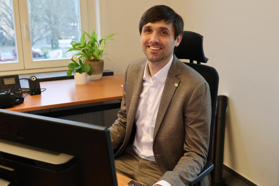 Dezernet Dirk Lange sitzt an einem Schreibtisch. Im Hintergrund ein Fenster, im Vordergrund ist der Teil des Bildschirmes zu sehen